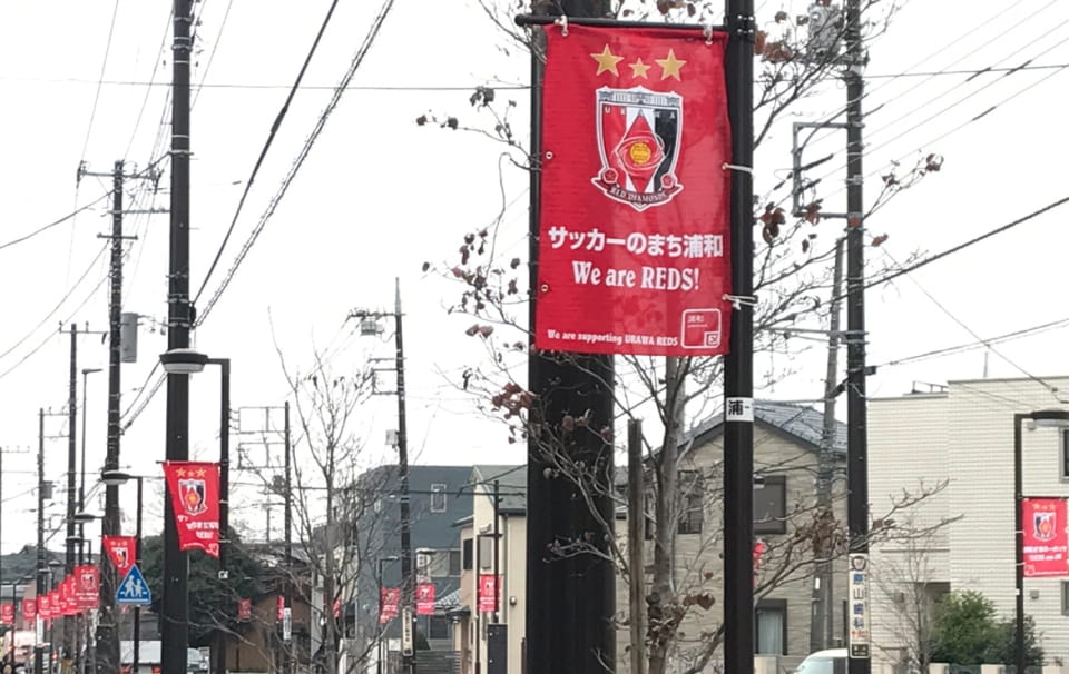 画像：浦和レッズロゴと「サッカーのまち浦和 We are REDS!」が書かれたバナーフラッグ